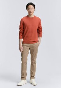 Maglione rosso a maglia, pantaloni beige e sneakers bianche. Il maglione presenta un collo rotondo e polsini a coste, mentre i pantaloni hanno una vestibilità dritta.