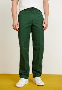 Pantaloni verzi din bumbac cu croi drept, dotati cu bucle pentru curea si inchidere cu nasture frontal, asortati cu adidași albi.