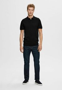 Svart kortermet polo skjorte med krage og tre knapper, kombinert med mørkeblå denimjeans og svarte slip-on sko.