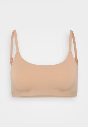 Soutien-gorge léger et sans coutures de couleur beige. Dispose de bretelles réglables et d'une texture lisse et douce sans rembourrage ni embellissements.