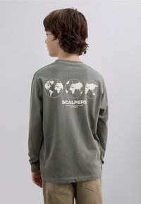 Långärmad olivgrön t-shirt i mjukt material. Har en grafisk design med tre världskartor och ordet "SCALPERS" nedtill.