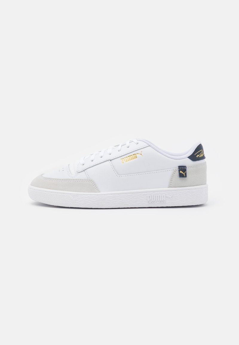 White sneaker with suede accents, featuring a textured rubber sole, gold logo, and navy heel tab. Classic low-top design.