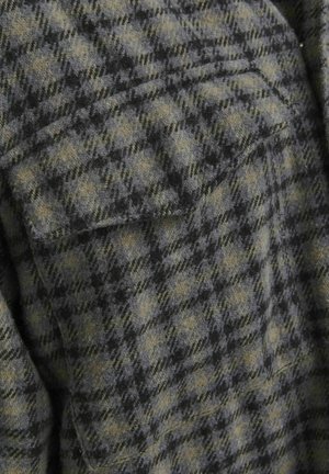 Wool shirt in woven check pattern with shades of grey and olive green. It has a textured feel and features a chest pocket detail.