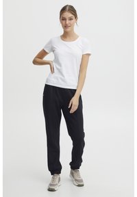 Hvit t-skjorte med korte ermer kombinert med svarte joggebukser med elastiske mansjetter, supplert med lys grå og beige sportsko.