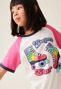 Hvid t-shirt med lyserøde ærmer, prydet med farverige rulleskøjtegrafikker og teksten "Super Star". Har en rund marineblå krave og en glat overflade.