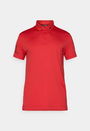 Polo rosso realizzato in un tessuto liscio, con colletto classico, tre bottoni e un accentuato motivo sulla manica sinistra.