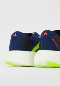 Pantofi sport albaștri cu un superior texturat, accente negre contrastante, talpă intermediară verde neon și detalii cu logo portocalii la călcâi.