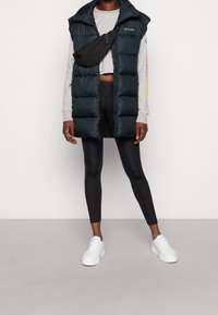 Puh na zimu v tmavě modré barvě s vysokým límcem, v kombinaci se šedou košilí s dlouhým rukávem, černými legínami a bílými teniskami. Obsahuje černou ledvinku.