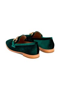 Mocasines de terciopelo verde oscuro con suelas de madera y detalle de cadena dorada en la parte superior, mostrados desde ángulos trasero y lateral.