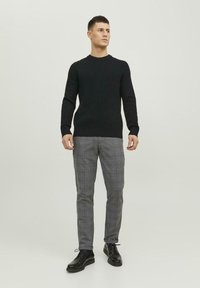Zwarte geribde trui, grijze geblokte broek met blauwe accenten, en zwarte veterschoenen; weergegeven op een neutrale achtergrond.