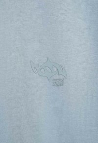 Jasnoniebieska bawełniana koszulka z gładką fakturą, z wytłoczonym wzorem płomienia oraz napisem "OPEN SOUL MIND" w kontrastowym kolorze.