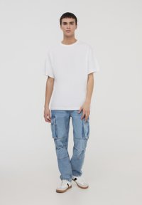 Biała koszulka z krótkim rękawem w zestawieniu z jasnoniebieskimi spodniami cargo z wieloma kieszeniami i luźnym krojem. Dopełniona białymi trampkami.