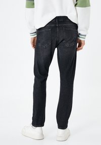 Jeans de mezclilla gris oscuro con un ajuste slim, que presentan dos bolsillos traseros y dobladillos ajustados, combinados con zapatillas blancas y una sudadera de color claro.