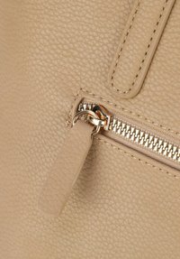 Sac en cuir texturé beige avec une fermeture éclair dorée, doté d'un tirette de fermeture éclair et de coutures renforcées près de la fermeture.