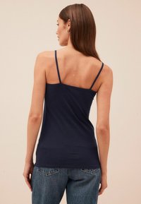 Top sin mangas de color azul marino con tirantes finos, hecho de tela suave, con un diseño ajustado y un escote en la espalda, combinado con jeans de lavado claro.