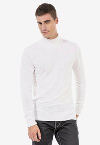 Pull en col roulé blanc avec un motif carré texturé, des poignets et un ourlet côtelés, design ajusté, associé à un jean noir.