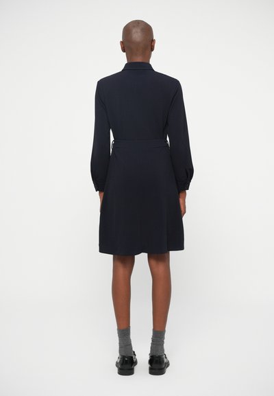 Tamsiai mėlyna suknelė su apykakle, ilgomis pūkuotomis rankovėmis, diržu liemenyje ir išplėsta apatine dalimi, pagaminta iš lygaus audinio.