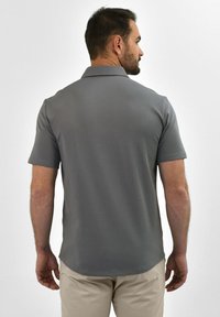 Grijze poloshirt met korte mouwen en een kraag, gladde textuur en een lichtgebogen zoom. Draagt bij beige broek, gezien van achteren.