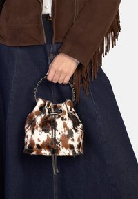 Mini bucketbag met bruine en witte vlekken, een gestructureerde afwerking, trekkoordsluiting en een metalen handvat met een tassel-detail.