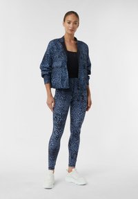 Set di giacca e leggings con stampa leopardata blu, realizzato in tessuto elasticizzato. Presenta una chiusura con zip, due tasche frontali e sneakers abbinate.