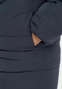 Jūrų laivyno pūkinė striukė, turinti lygią, blizgią išorę, laisvą siluetą ir šonines kišenes, sukurta šilumai ir komfortui.