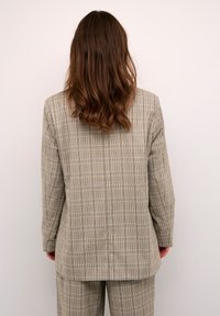 Blazer de cuadros beige con diseño a medida, con líneas sutiles en azul. Hecho de una tela ligera con una textura suave.