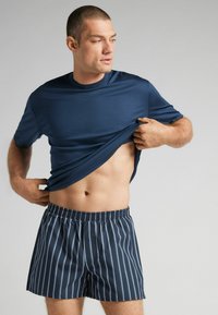 Navy modrá polokošile s krátkým rukávem vyrobená z hladké tkaniny; doplněná o modré pruhované kraťasy s elastickým pasem a rovnom střihem.