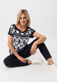 Korte mouwen top met een geometrisch zwart-wit patroon, gecombineerd met donkere broeken en witte sneakers, die een relaxte pasvorm en modern ontwerp laat zien.