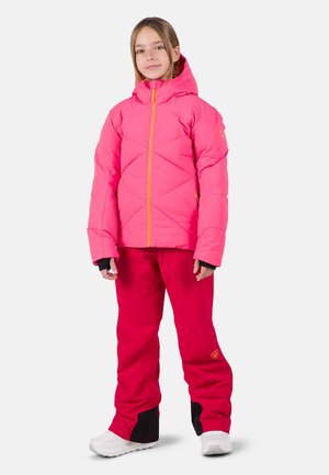 Helle pinke, gepolsterte Jacke mit diagonaler Steppung und orangefarbendem Reißverschluss, kombiniert mit roten Hosen mit schwarzen Akzenten und weißen Schuhen.