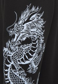 Tessuto nero con una grafica dettagliata di un drago blu con scaglie intricate, baffi e criniera fluente, centrata su una manica.