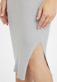 Graues, geripptes Strickkleid mit einem seitlichen Schlitz und strukturiertem Stoff. Der Saum ist schräg geschnitten, was das figurbetonte Design hervorhebt.