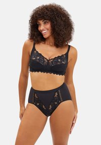 Zwarte kanten bralette met een geschulpte rand en transparante details, gecombineerd met zwarte high-waisted onderbroeken met kanten accenten en uitsnijdingen.