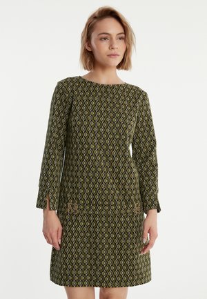 Groene jurk met patroon, lange mouwen, ronde halslijn en zijsplitsingen, met een geometrisch ontwerp in geel en zwart, geaccentueerd op de taille.