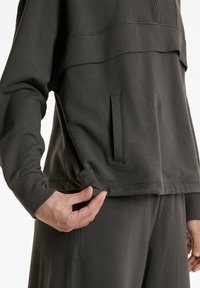 Dunkelgrauer Sweatshirt mit einem Viertel-Reißverschluss-Halsausschnitt, Fronttasche und strukturiertem Saum. Das Material wirkt weich und flexibel.