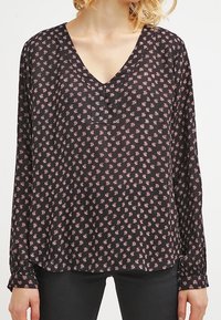 Blouse noire à manches longues avec un décolleté en V profond, présentant un petit motif floral rose. Fabriquée en tissu léger et semi-transparent.