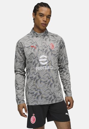 Pull en gris avec un motif camouflage, doté d'un col à demi-zip, d'accents rouges et d'un logo sur la poitrine et les shorts. Texture lisse.