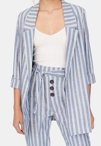 Pasiasty niebiesko-biały żakiet z długimi rękawami, zestawiony ze spodniami w kolorze dopasowanym o wysokim stanie z zapięciem na sznur i guzik.