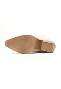 Suela de zapato beige con una superficie de goma texturizada, diseño inclinado y un ligero tacón. Incluye patrones acanalados para mayor tracción.
