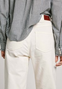 Pantalones de pana blancos con bolsillos traseros, combinados con una camisa a cuadros azul y blanca. La camisa tiene puños abotonados, visibles debajo de la chaqueta.