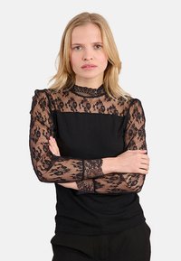 Top nero con maniche lunghe in pizzo a motivo floreale, design a collo alto e texture a costine sul corpo. Trasmette un look stratificato.
