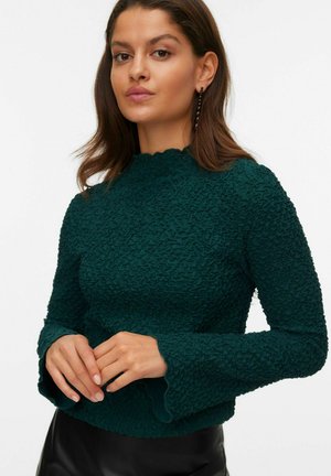Temno zelena majica z textured pletenjem, okroglim izrezom in razširjenimi dolgimi rokavi. Ima valovite robove na izrezu in manšetah.