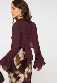 Blusa burdeos con mangas acampanadas, que presenta una tela fluida y un diseño de espalda en capas, combinada con una falda de estampado floral.