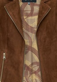 Bruine suede leren jas met een slank ontwerp, asymmetrische ritssluiting en een beige voering met patronen van ronde motieven in kastanjebruin en geel.