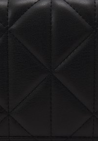 Cuir noir matelassé avec une surface texturée, présentant un motif géométrique en losanges et des surpiqûres contrastantes.