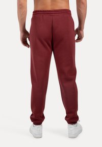 Bordeauxfarvede sweatpants med elastisk talje, der har en glat overflade og afslappet pasform, kombineret med hvide sneakers.