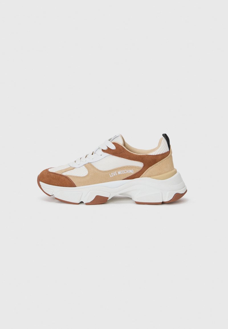 Kratki športni čevlji z mešanico bež mrežaste tkanine, rjavimi usnjenimi detajli in belim gumijastim podplatom. Imajo logo in kontrastni črni jezik.