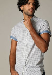 Korte mouwen button-up shirt in het wit met een geometrisch patroon. Beschikt over denimaccenten bij de mouwen en een klassieke kraag.