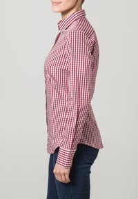 Punainen ja valkoinen ruudullinen paita, jossa on kauluksellinen kaula-aukko ja kapeat siluetit. Napitettu hihansuu ja sivuhalkiot tuovat lisää yksityiskohtia.