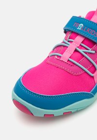 Ροδοκόκκινο αθλητικό παπούτσι με μπλε λεπτομέρειες, διαθέτοντας ένα ανθεκτικό λουράκι, υφασμάτινη άνω επιφάνεια με υφή και εύκαμπτη σόλα σε τυρκουάζ και ροζ.