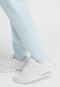 Pantalones de chándal azul claro con puños de canalé, combinados con zapatillas Nike Air Max blancas que presentan una parte superior de malla y piel, con amortiguación de aire visible.
